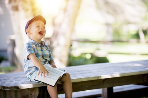 Image of young boy sitting on a park bench laughing wildly.