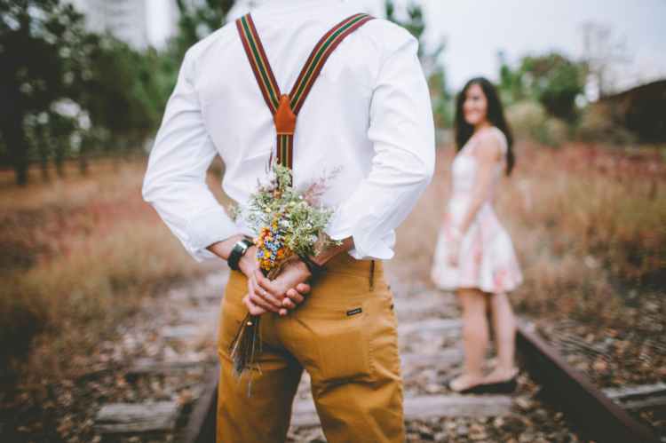 Happiness image of young man and woman.  Man has a bunch of flowers hidden, waiting to give to woman.