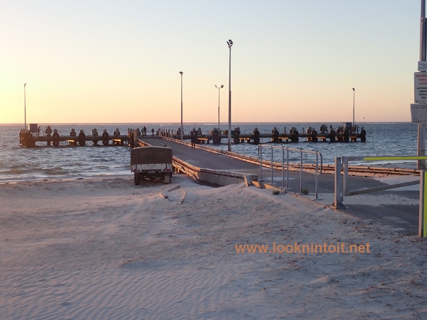 Picturesque scene of Beach with tee shaped jetty and the setting sun slightly visible in left of image.  Beach is white sand.